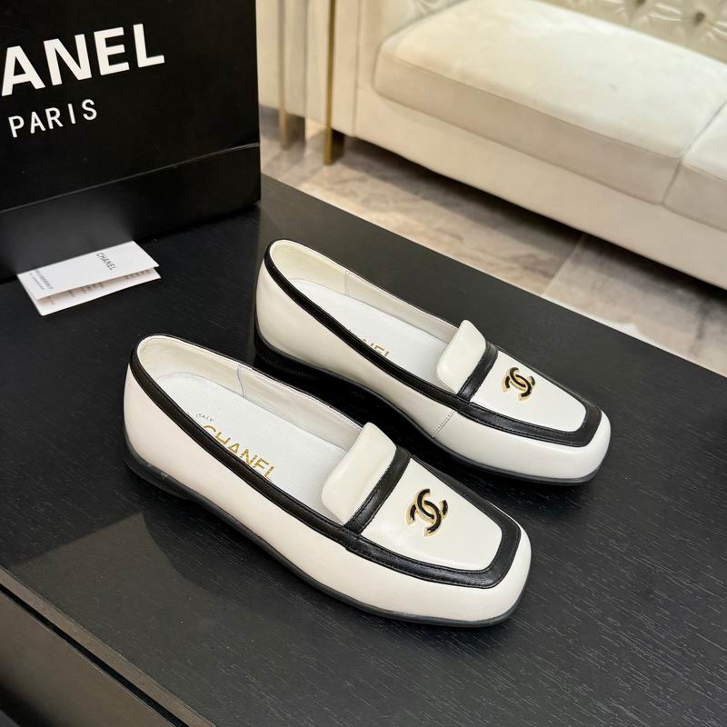 Chanel CC Logo Bicolor Leather Loafers in cream and black displayed on a dark surface next to Chanel box